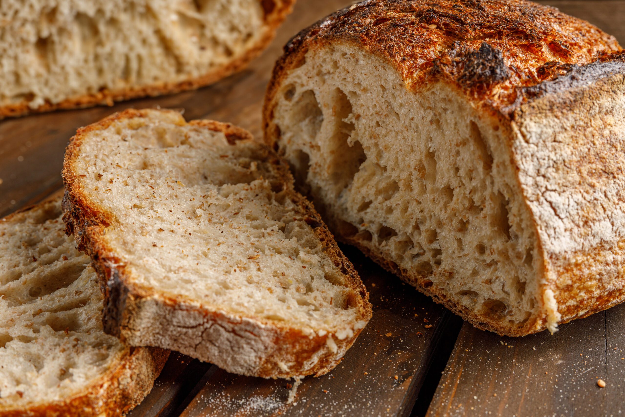 Artisanal Bread resting on a Wooden Surface with a beautifully Sliced Loaf Displayed beside it Organic Sourdough - Image 1